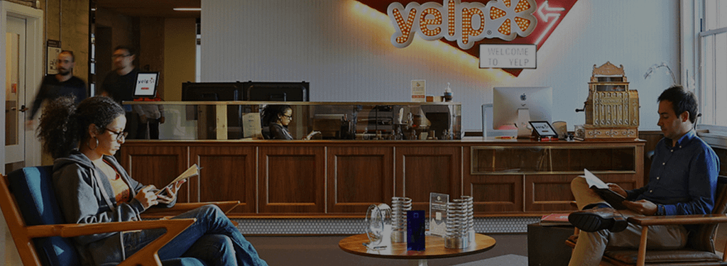 Two people sitting in a corporate lobby reading. Yelp sign on the wall.