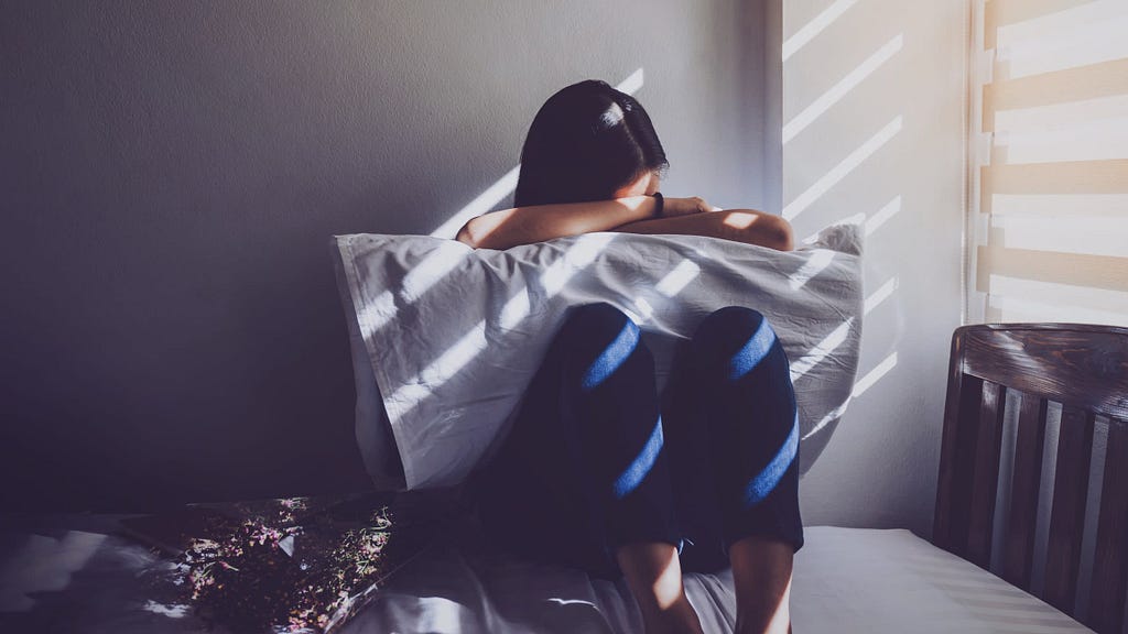 woman sitting on bed with head in pillow.