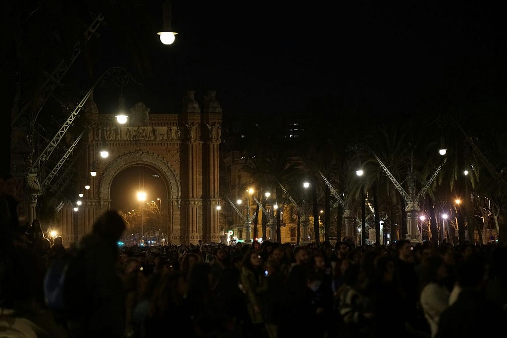 a crowd of people standing in front of a building at night. 8.03.2023, Barcelona, Spain. Crowd of people protest at Barcelona’s Arc de Triomphe