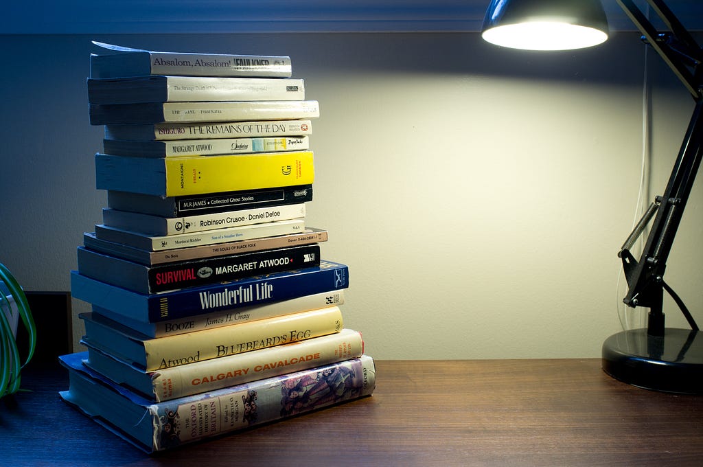 A stack of books on a desk, lit by a desk lamp