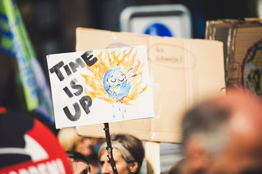Global warming protest sign saying “Time is up” and a burning planet earth