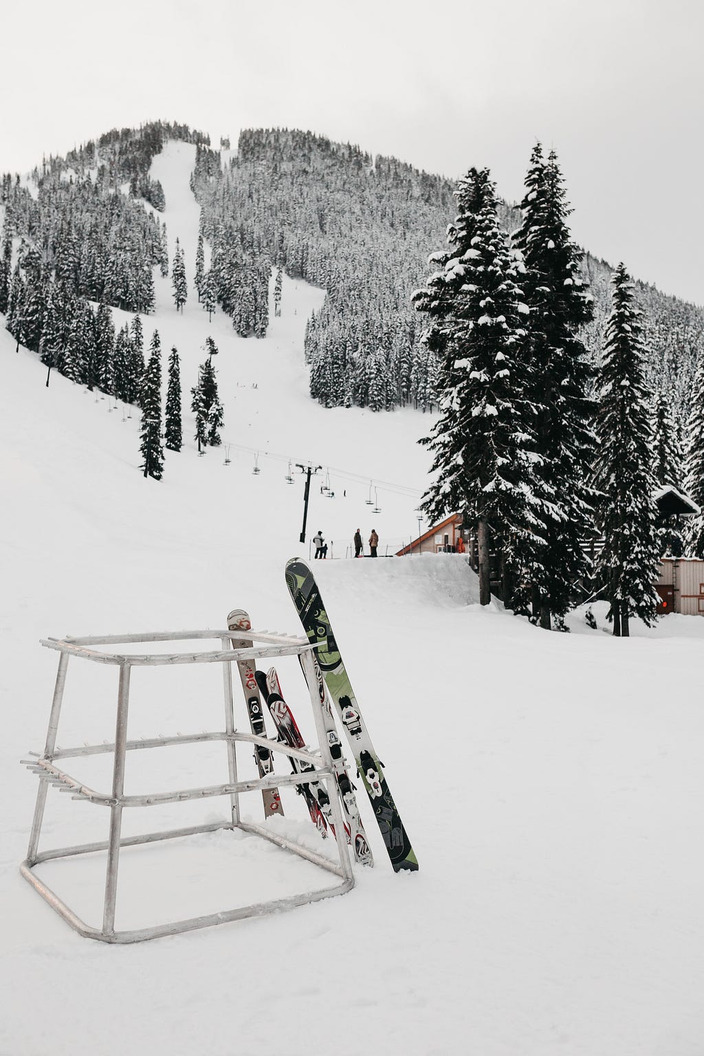 Skis on a stand in front of a snowy ski slope and pines trees.