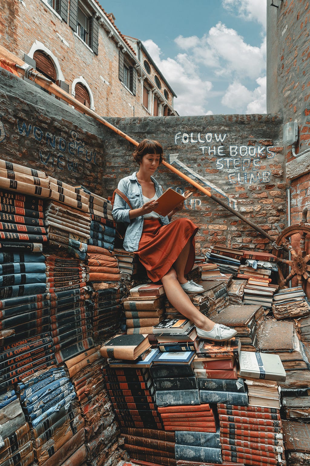 a woman in an alley sitting on a lot of books and reading