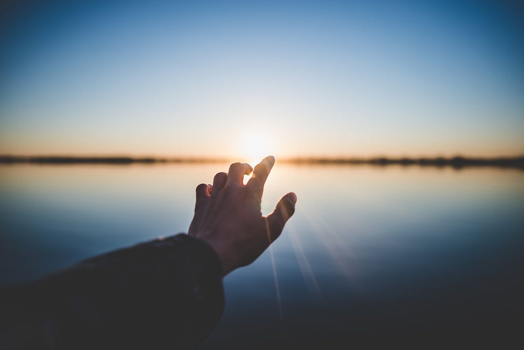 Hand reaching out to a sunrise over a lake
