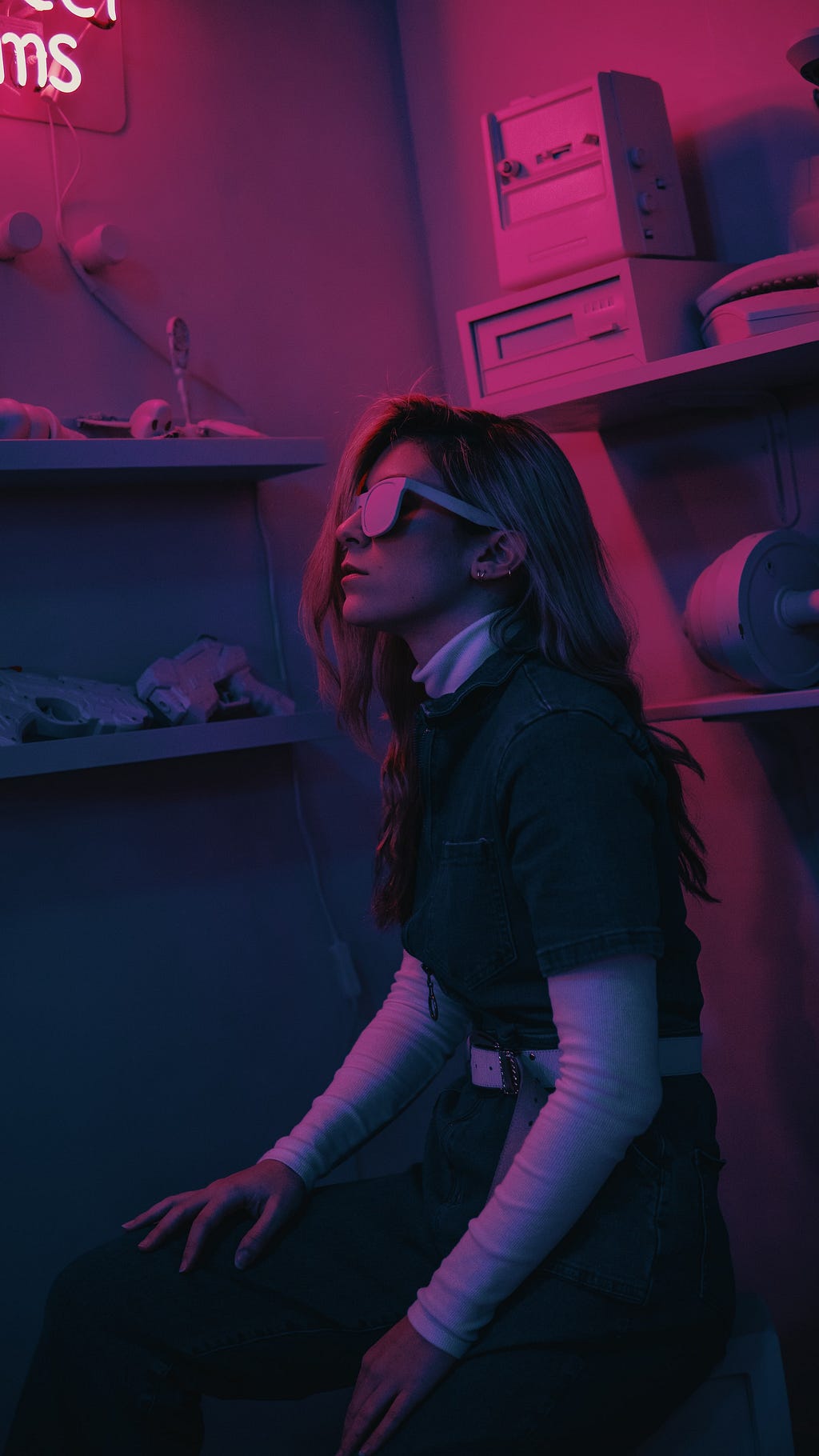 Fururistic cyberpunk style image in a pink tone of a woman with sunglasses in a room, kneeling and looking up.