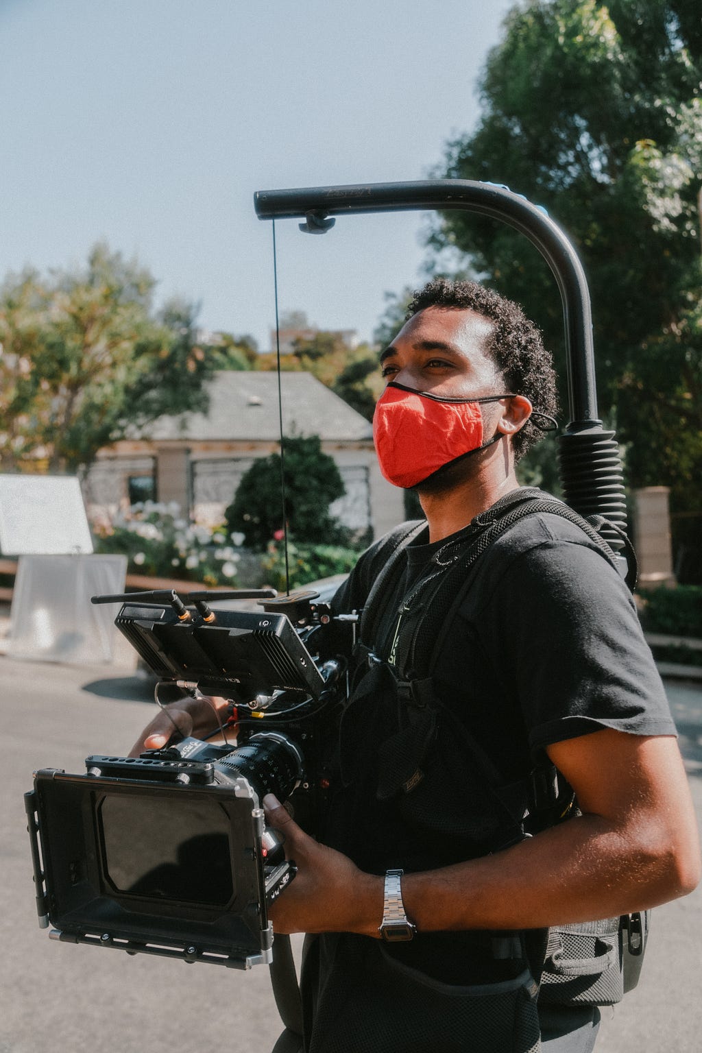 image of a Black man with audio/visual recording gear. He is wearing a face covering and is standing outdoors.
