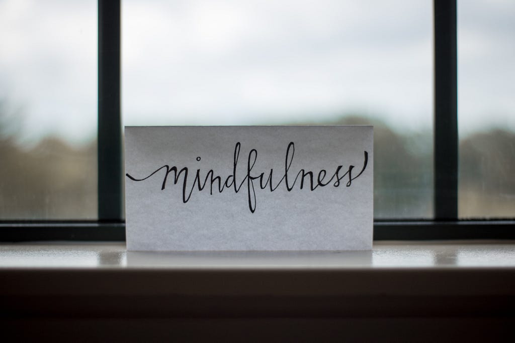 Piece of paper that reads mindfulness propped on a window sill by a window