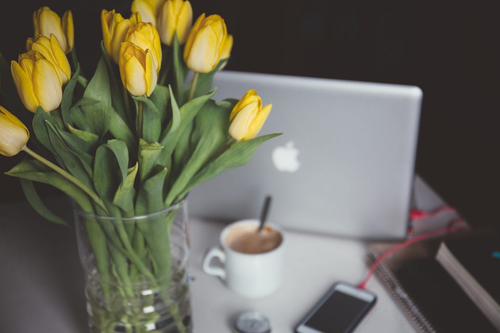 Yellow tulips on desk, next to laptop, mobile phone and coffee cup