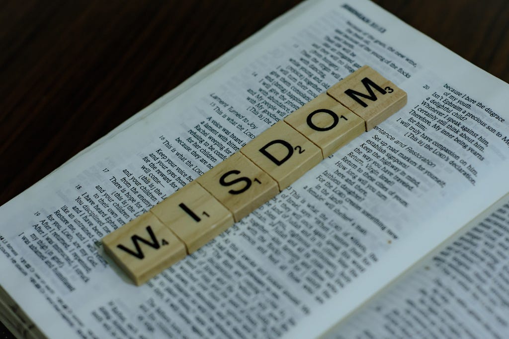 An Unsplash photo by Alex Shute showing Scrabble tiles spelling “Wisdom” laying on a Bible.