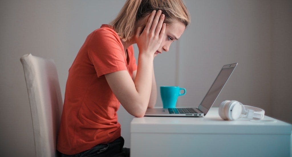 A distraught woman holding her face in her hands while looking at her laptop