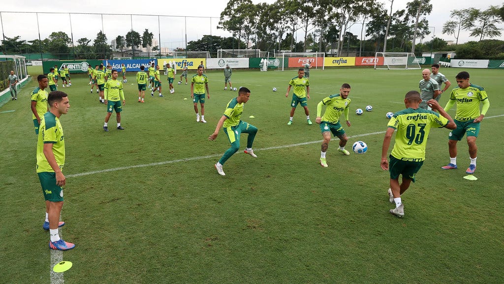 Jogadores do Palmeiras treinam no CT, vestindo camisa verde limão com detalhes em verde escuro, cação verde escuro e meias brancas. há cerca de 20 jogadores na foto, divididos em pequenas rodas e tocando bola