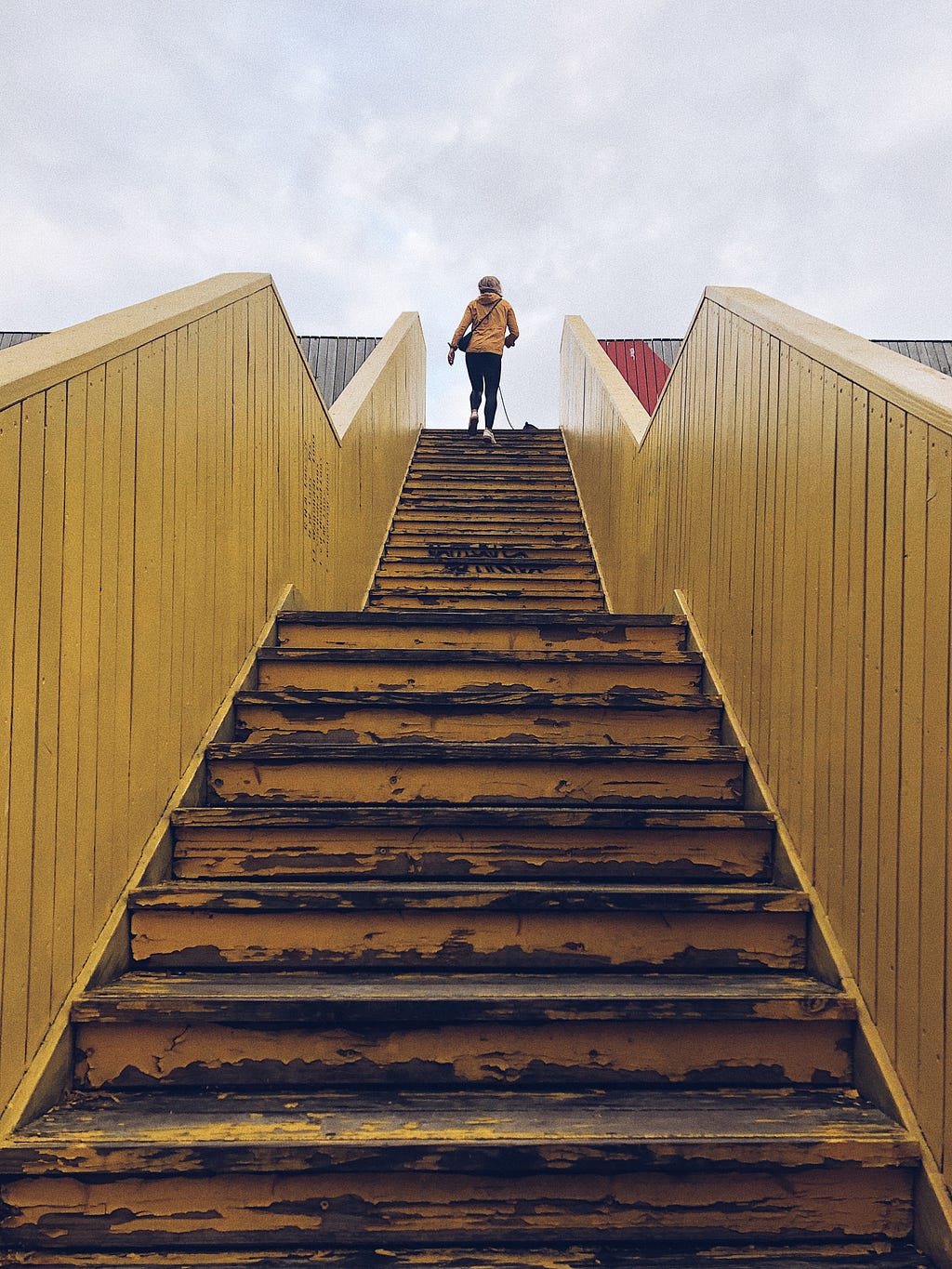 A woman dressed in yellow climbing the stairs. The stairway is also painted yellow
