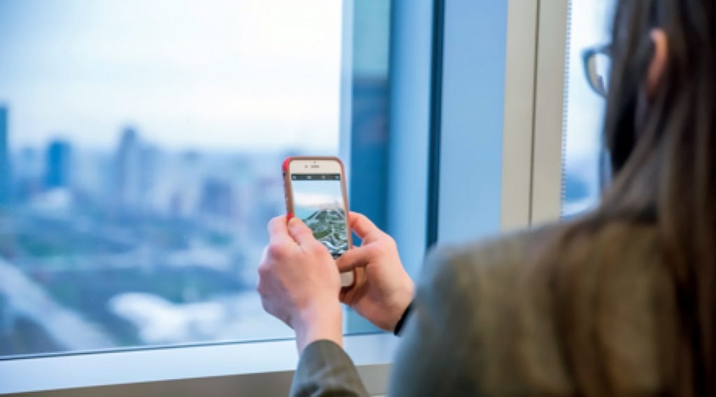 Bridget holds her phone up to the window to take a photo of Millenium Park from the Blue Cross Blue Shield IL building.