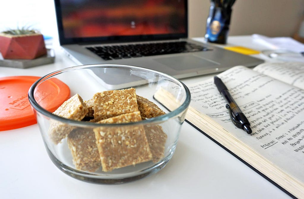 ginger turmeric bone broth protein bites in a glass container next to an open notebook and a computer