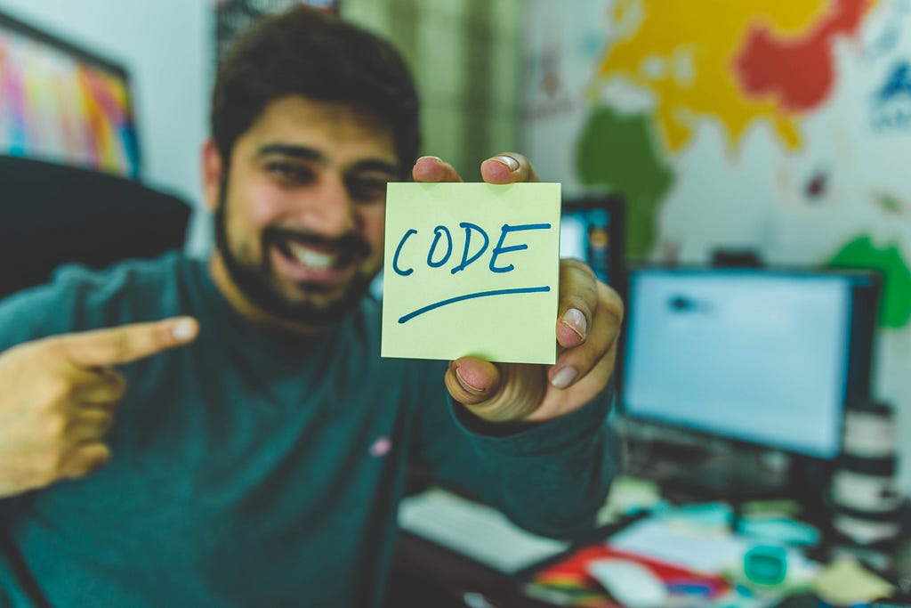 A man holding a note that writes code shows the paper with his other hand.