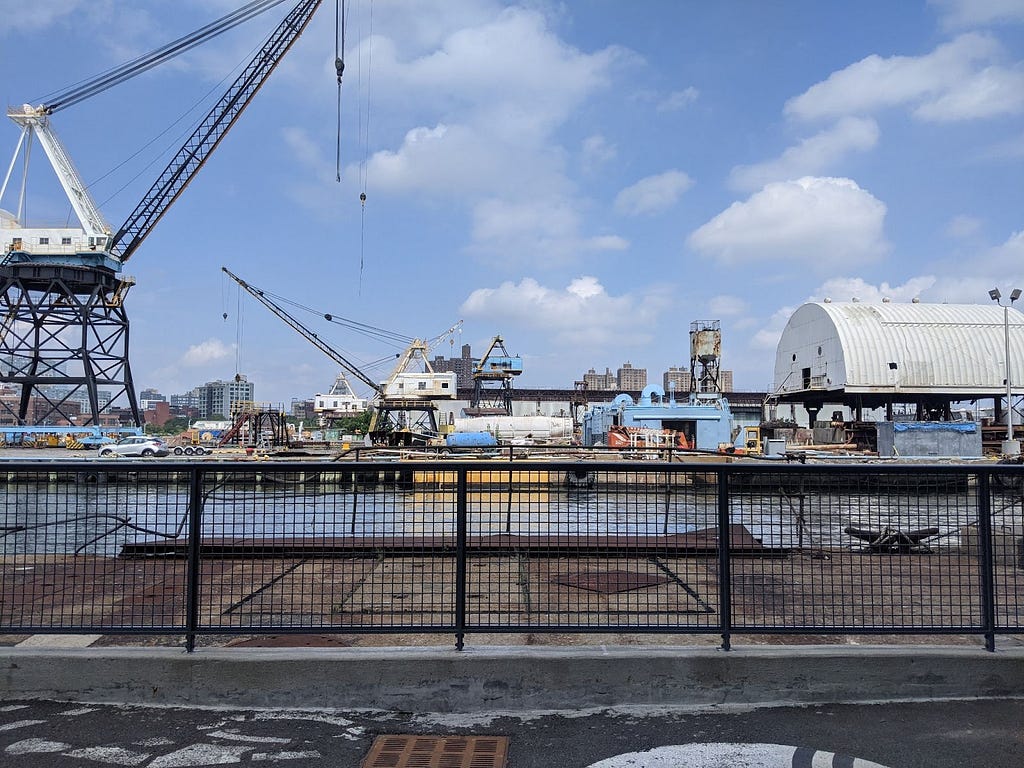 A photograph of a heavily-used industrial area by the water, filled with cranes, boats, and warehouses.