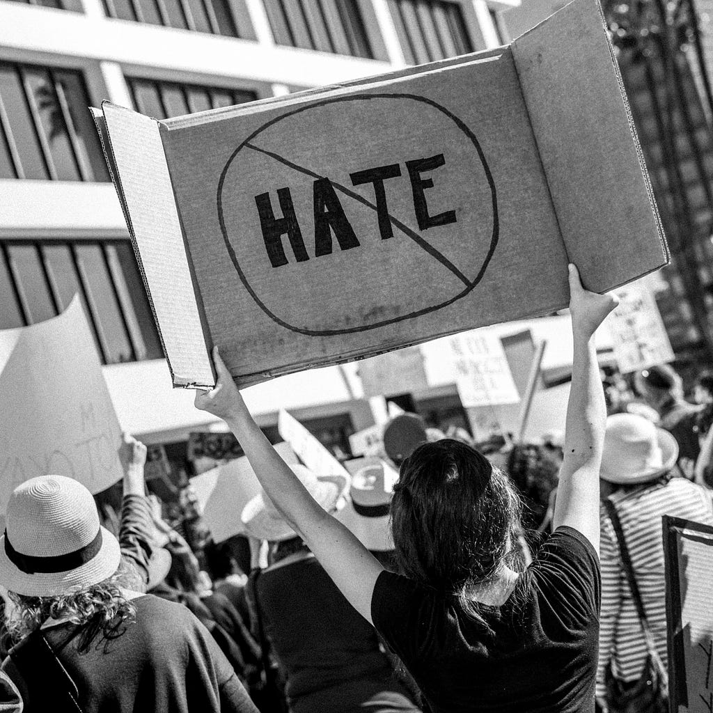 Person holding a poster with the word “HATE” crossed out, as hate shouldn’t tolerated