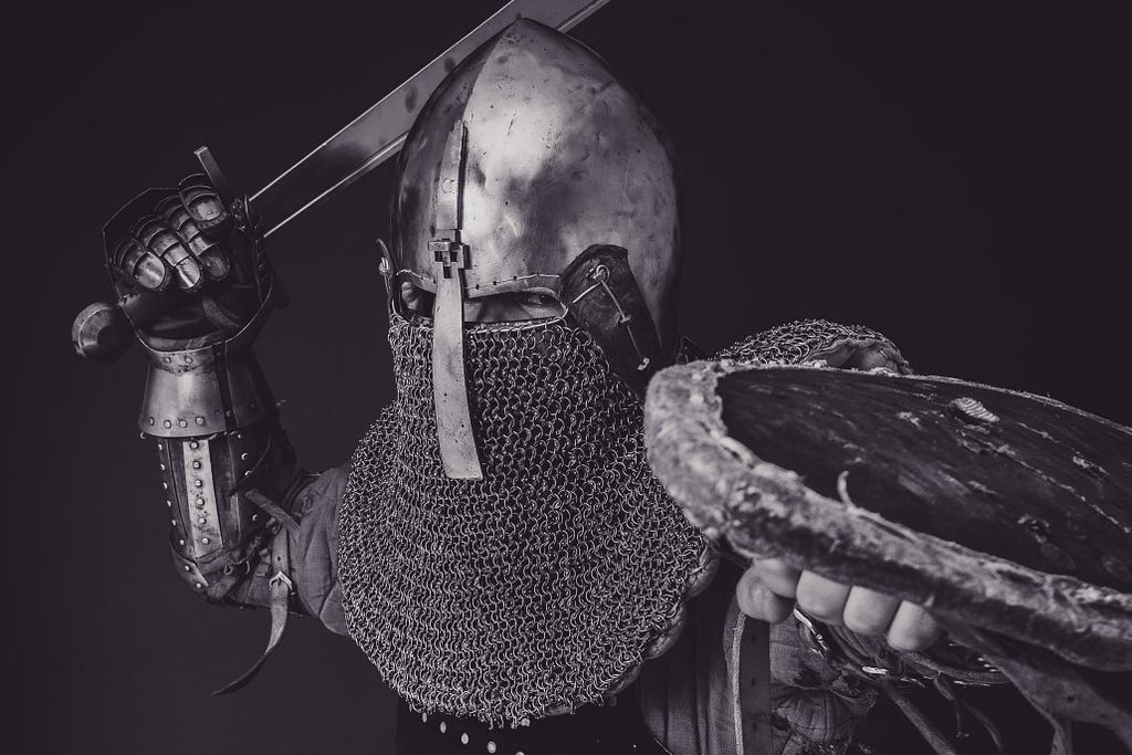 Um guerreiro escondido completamente em uma armadura ergue a espada e o escudo