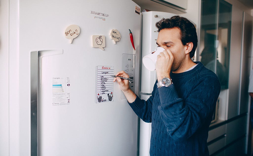 Image of a man writing his weekly goals on a fridge planner