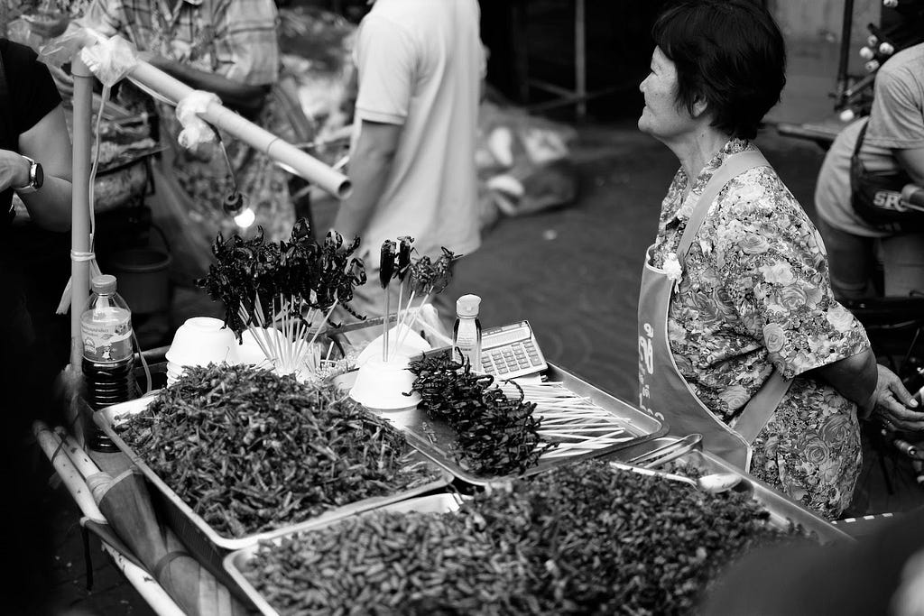 A woman standing in front of fried insects, which are popular Thai snacks.