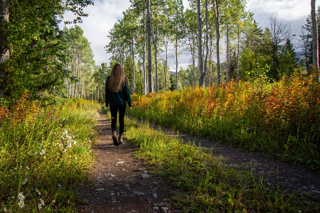 This image depicts a woman walking along a path in a forest.