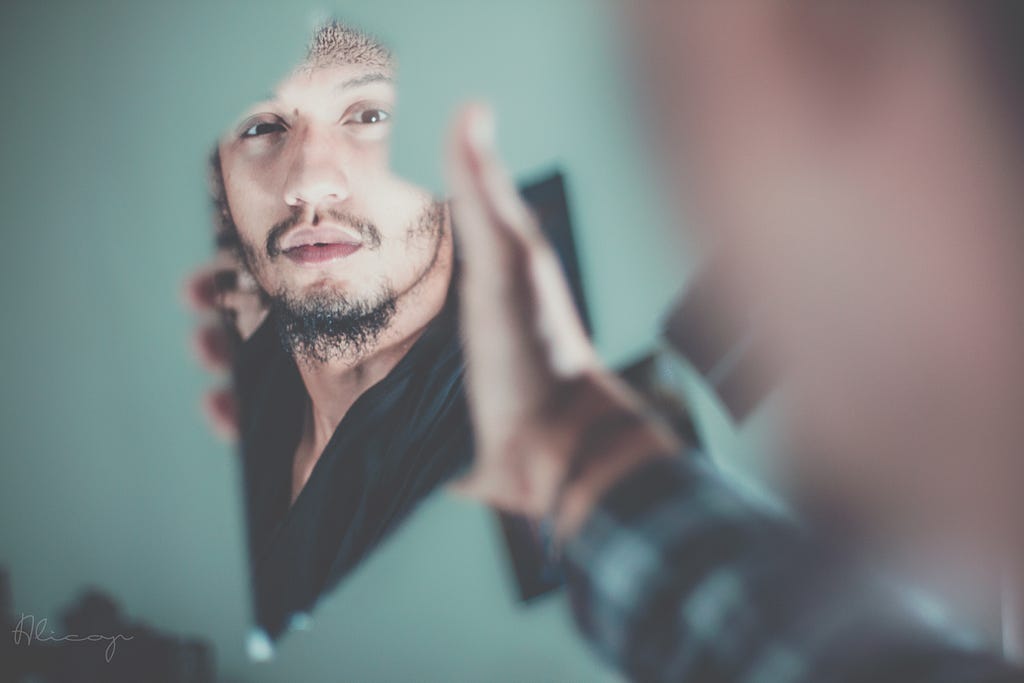 A man holding a shard of a mirror looking at the reflection