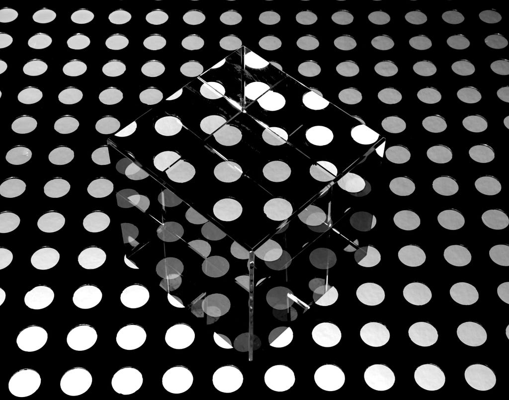 White polka-dots on a black background. There is a reflective metal square in the center, with the polka-dots reflecting off the metal so that the pattern is slightly disrupted.