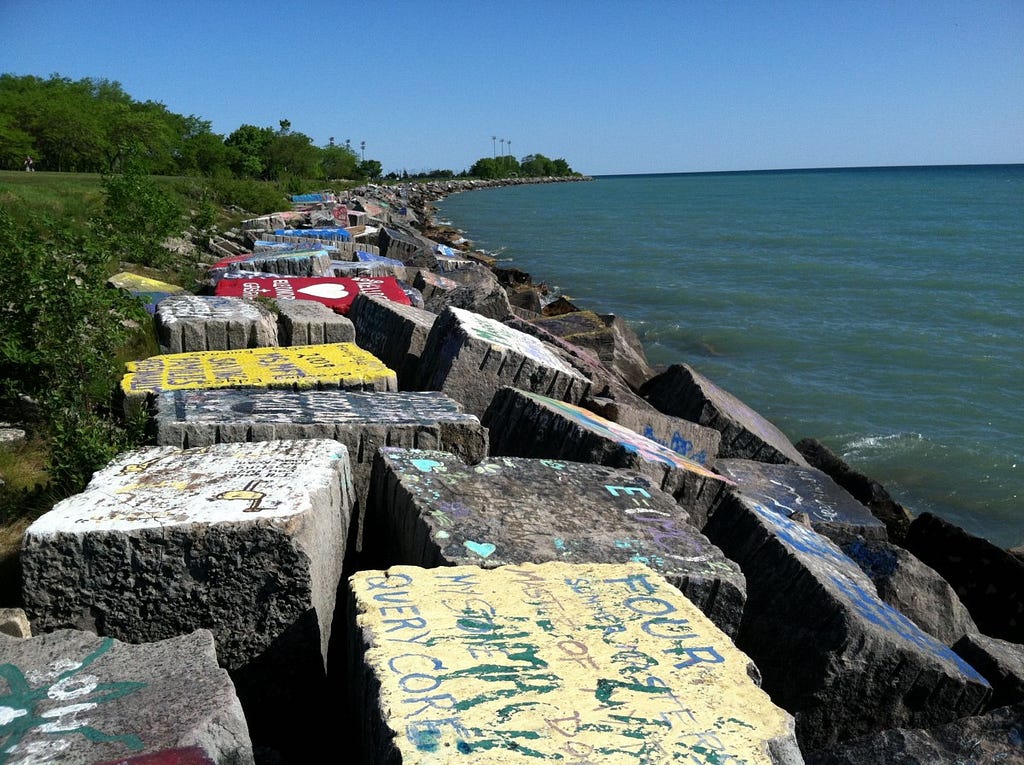 A photograph of large chunks of concrete — each covered in vibrant graffiti — lining the shore of Northwestern University’s “Lakefill,” the place where south campus meets Lake Michigan.