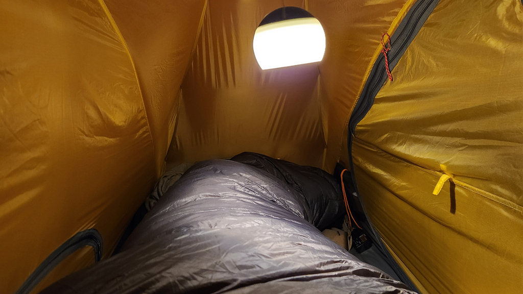 Inside a small tent just big enough for a sleeping bag, with a lamp hanging from the roof