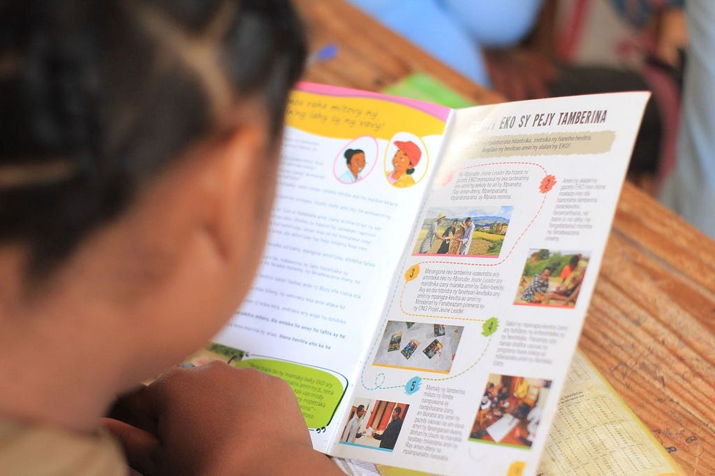 Looking over the shoulder of a student at the magazine they are holding, in Madagascar. The page of the magazine is slightly out of focus.