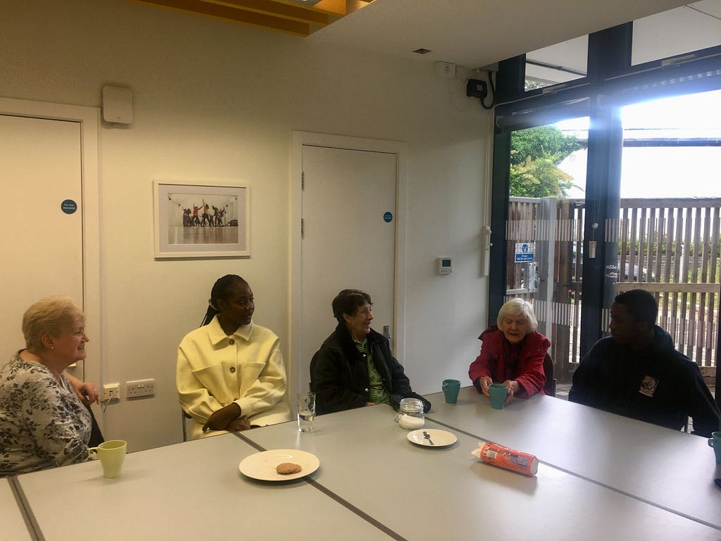 Five people sat around a table with mugs, biscuits and plates on the table