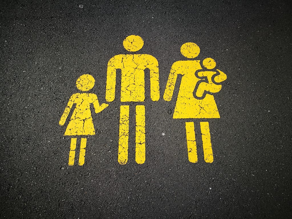 Painted figures of a family (mother, father, toddler and small child) in yellow on a road.