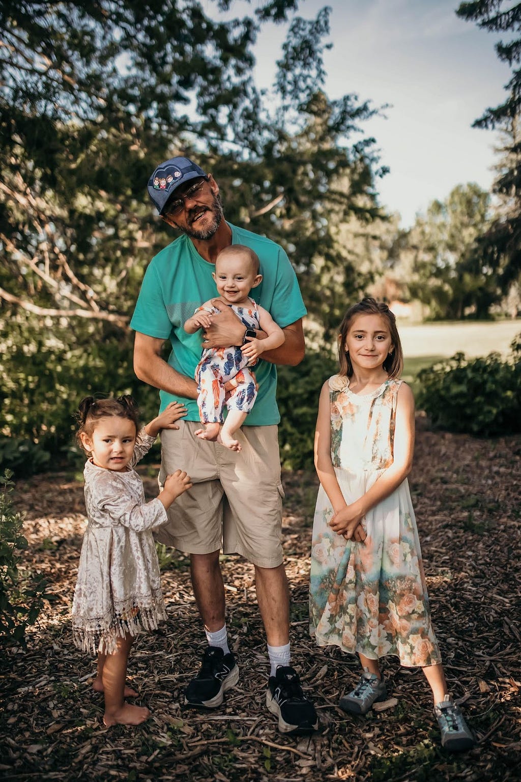 Man holds smiling baby outside while young children look at the camera