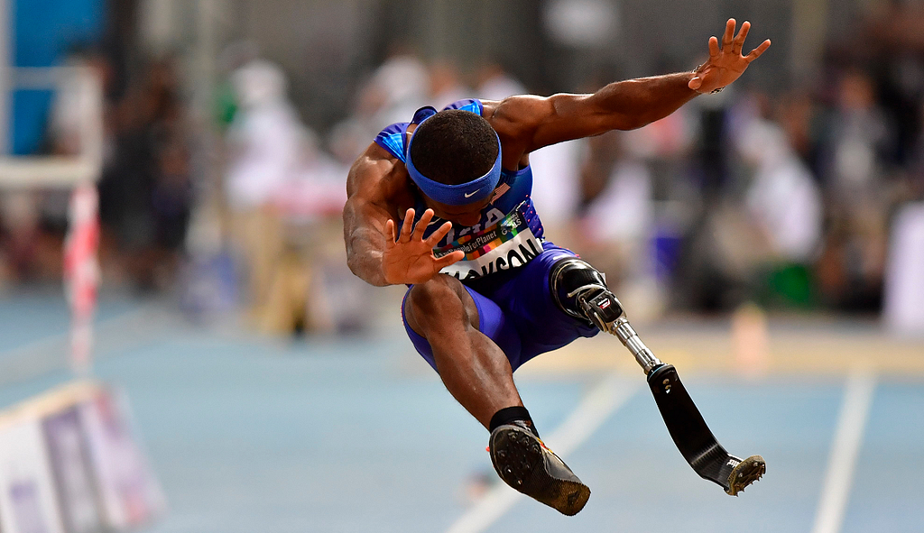 Paralympian male athlete jumping with head done and arms and legs out stretched — on leg is a prosthetic blade