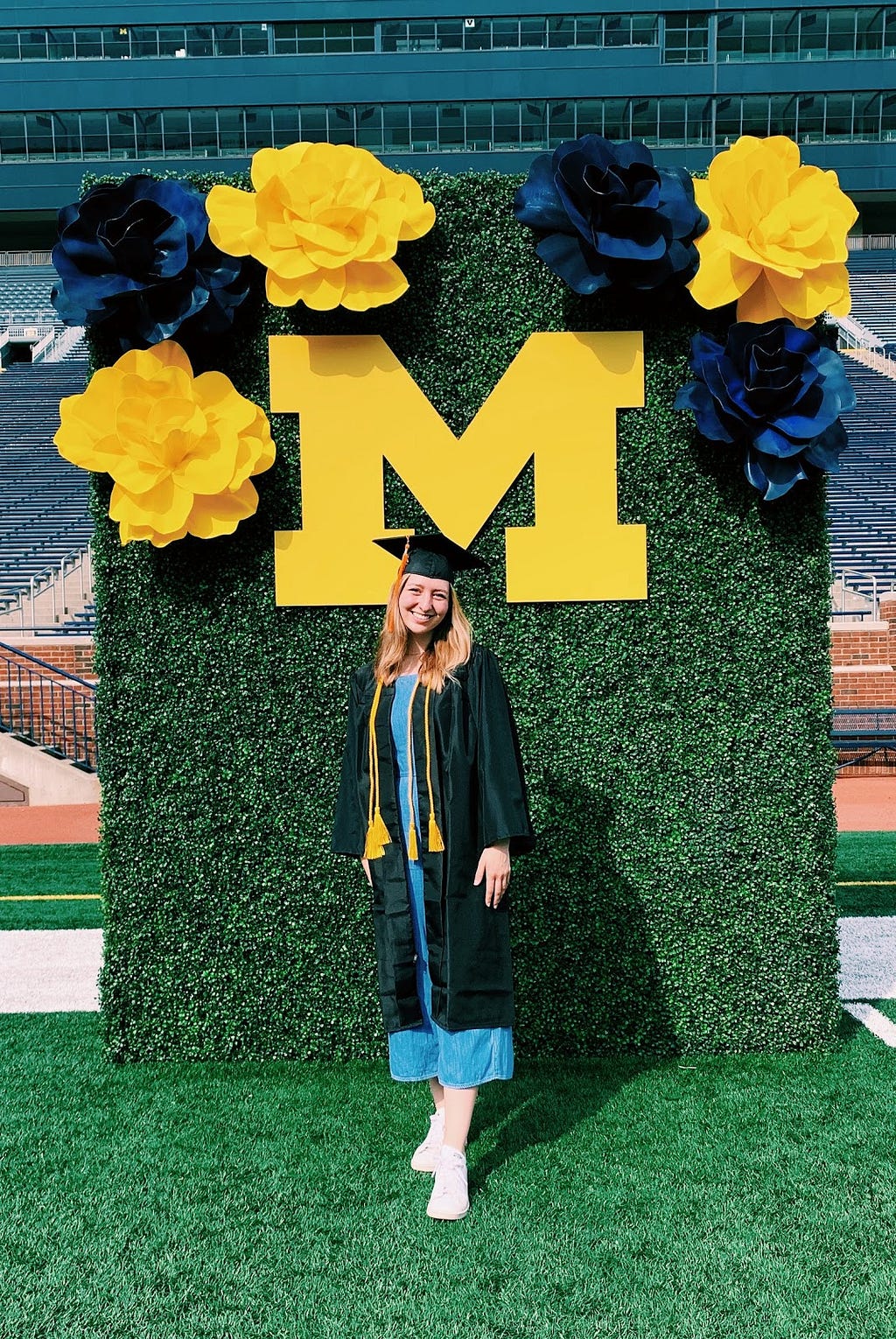 Allie stands in a graduation cap and gown in the Big House