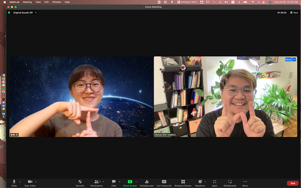 A screenshot of a Mac computer with a fullscreen Zoom meeting window. The window is divided into two camera screens with Yenching on the left and Munus on the right. Yenching has straight bobbed hair, round glasses and a gray t-shirt smiling at the camera with a background of space and stars, posing a letter T with her hands. Munus has bleached hair with a curvy bang and wears round glasses and a black t-shirt.