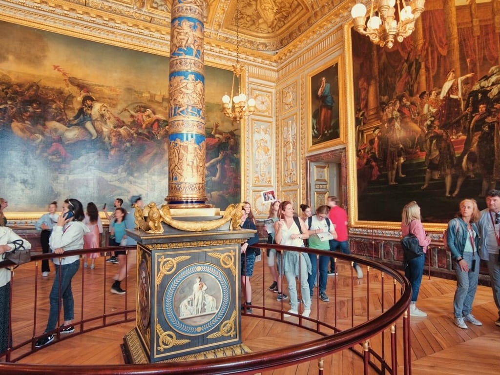 A group of people standing in an ornate room with paintings on the walls.