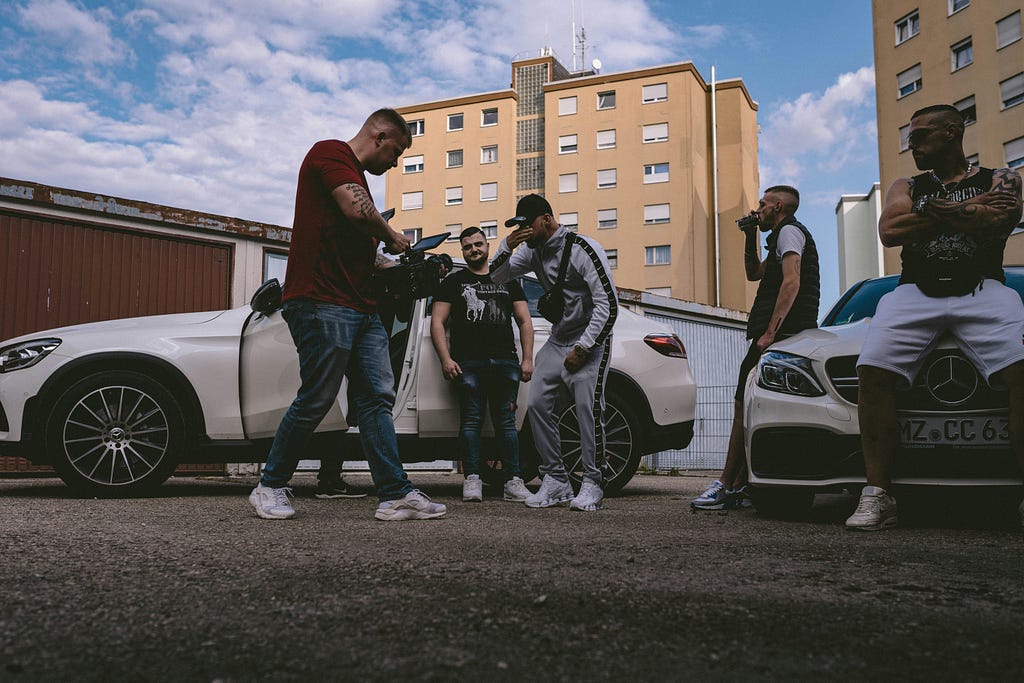 Picture of a bunch of gangsters gathered round a car via Alt text on Medium