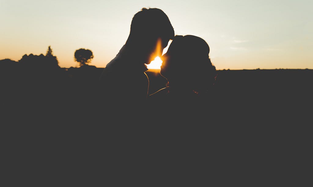 silhoutte of man and woman in a field with a tree visible in the distance