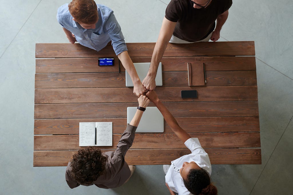 A group of four colleagues standing around a table and touching their fist together.