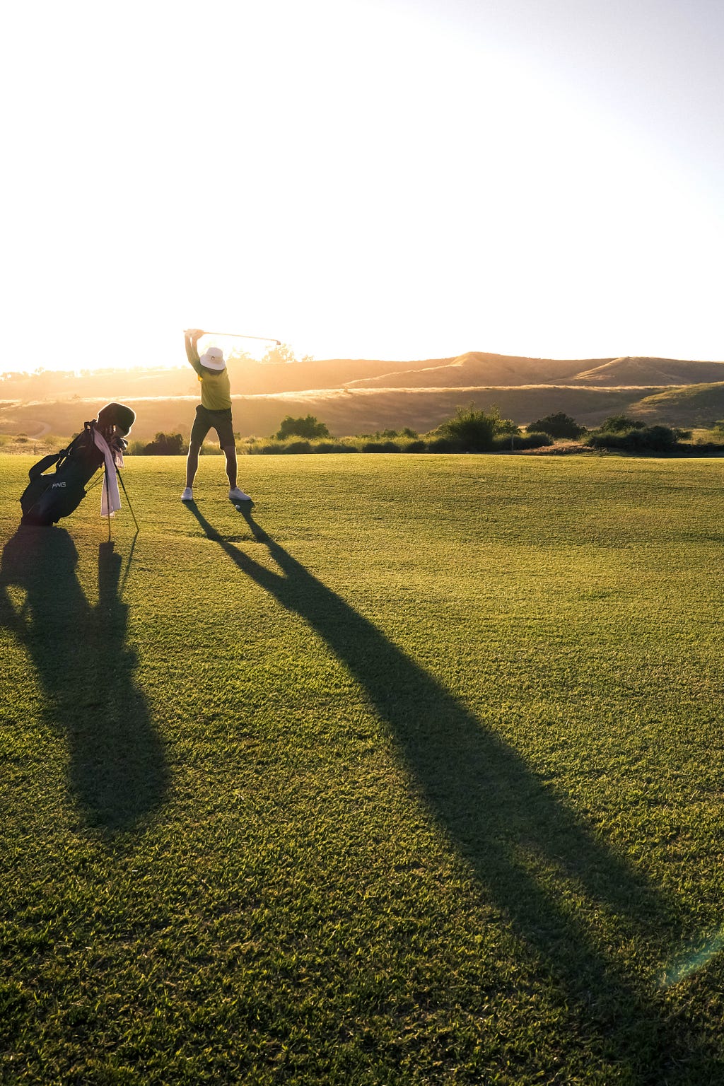 A golfer hitting a long iron as the sun sets.