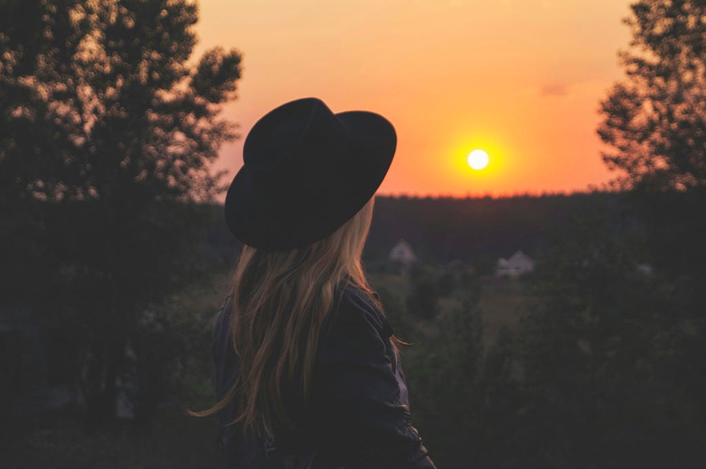 Woman wearing black hat, gazing at sunrise.