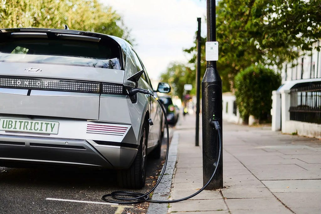 Electric vehicle connected via cable to a lamp post charge point on street