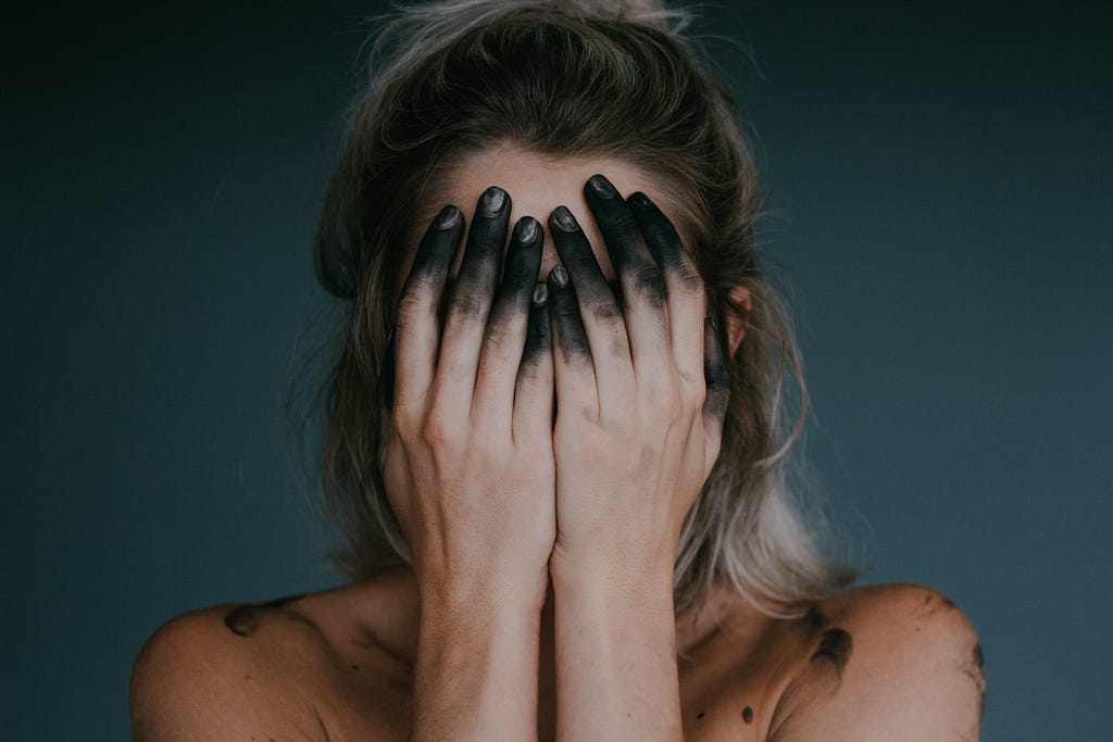 Image of a woman covering her face with black-stained fingertips.