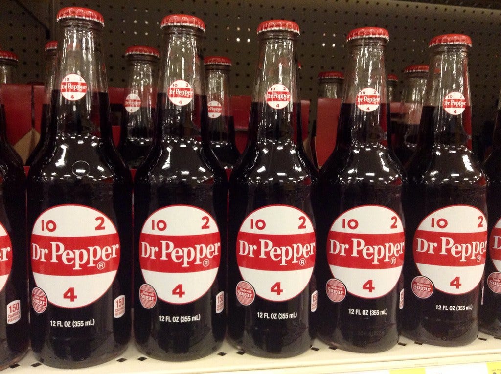 A photograph of some olde-timey Dr. Pepper bottles in a shop. The glass bottles are a throw-back, retro design with 1960’s style labels.