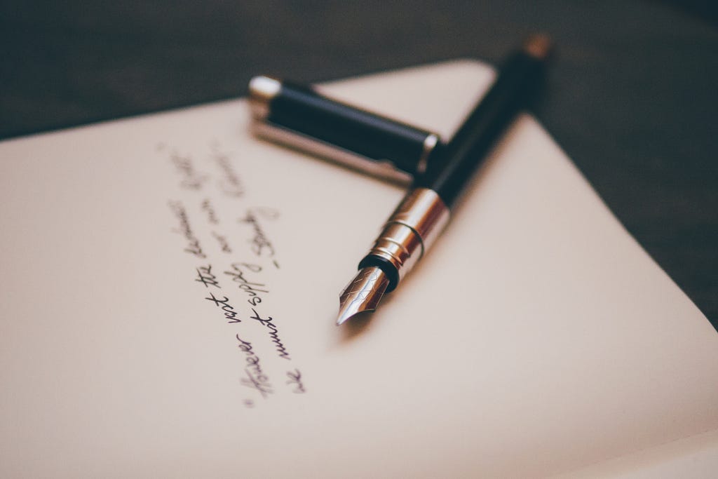 A fountain pen atop a notebook with a blurry quote written on it.