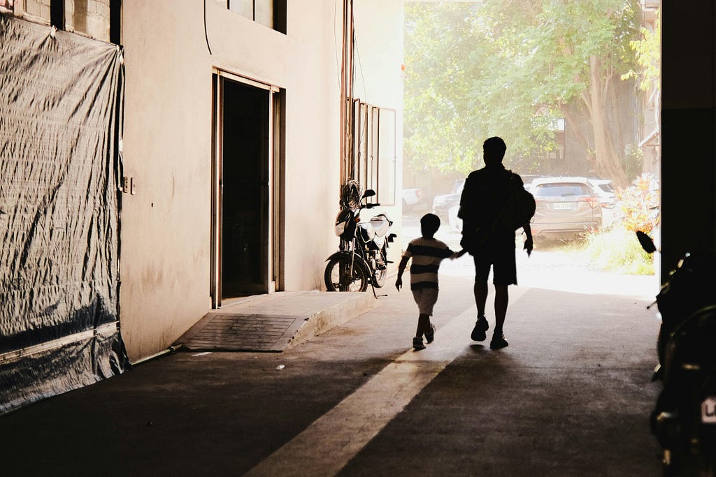 Man and boy walking in an alley next to a building.