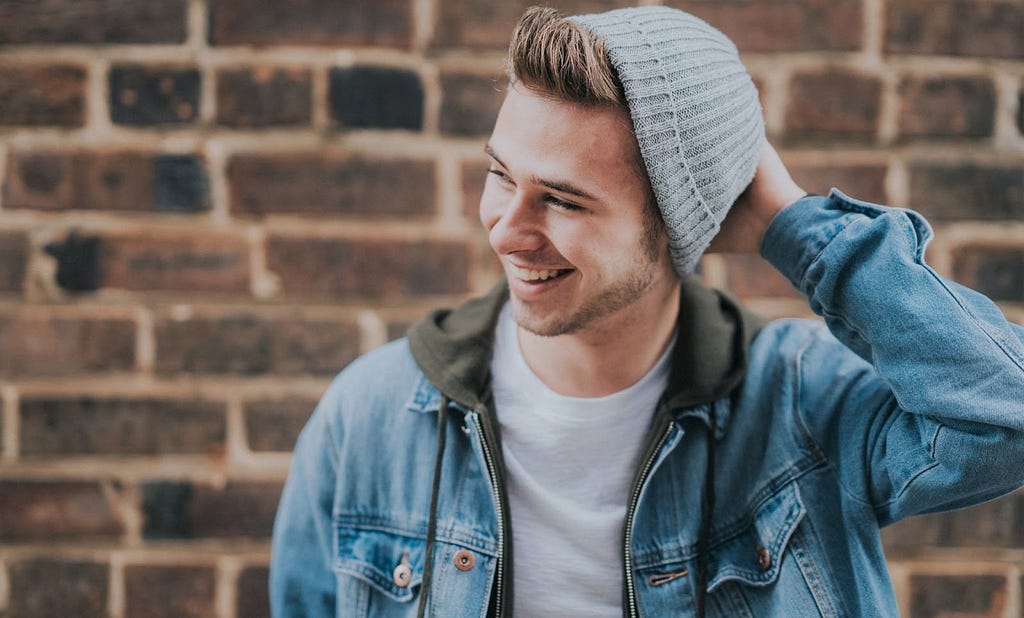 A smiling man wearing a beanie and a denim jacket