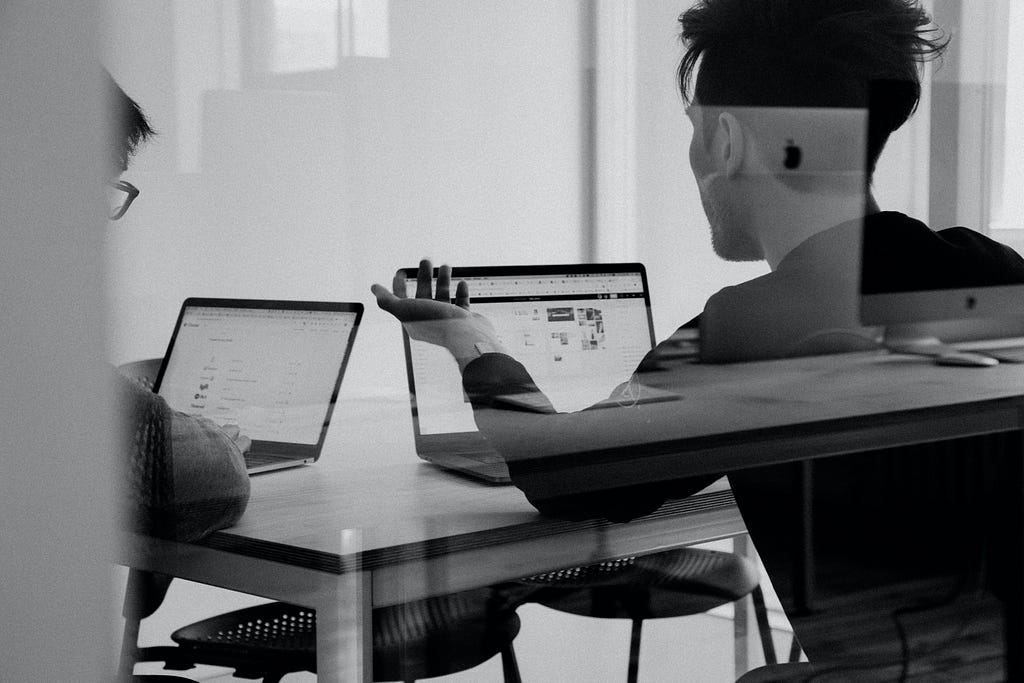 Two people with laptops open talking at a table.