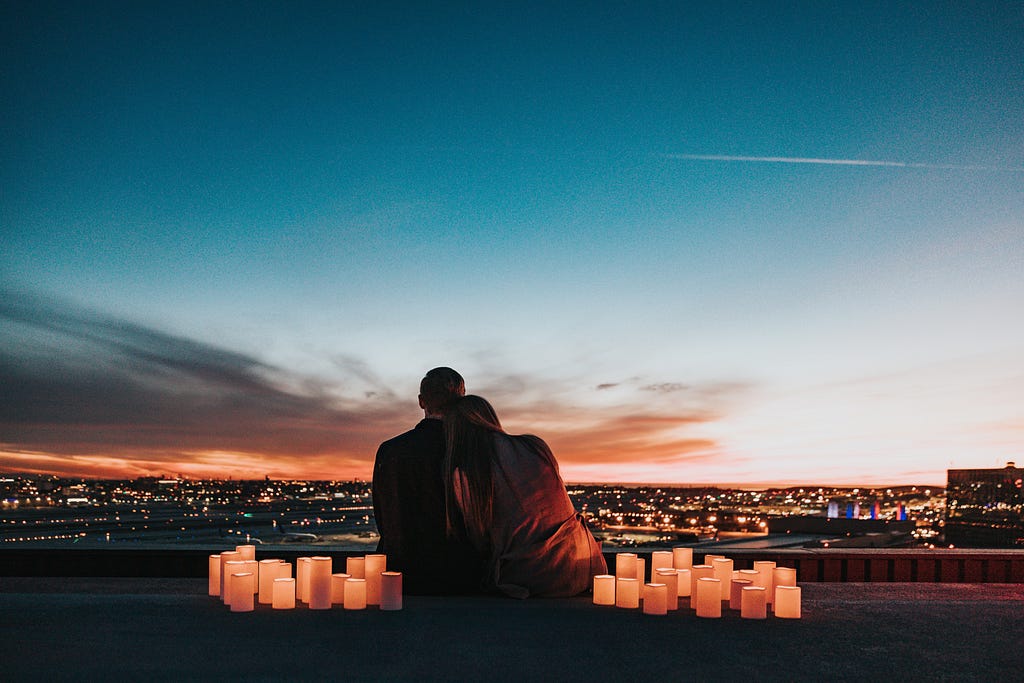 A couple overlooks a city at dusk